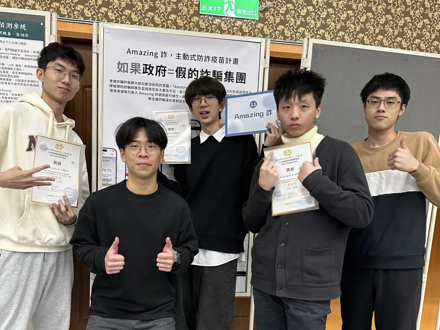The team holding certificates in front of the “Amazing 詐” poster